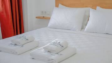 A neatly made bed with white linens and towels, a wooden headboard, and a small shelf with a power outlet.