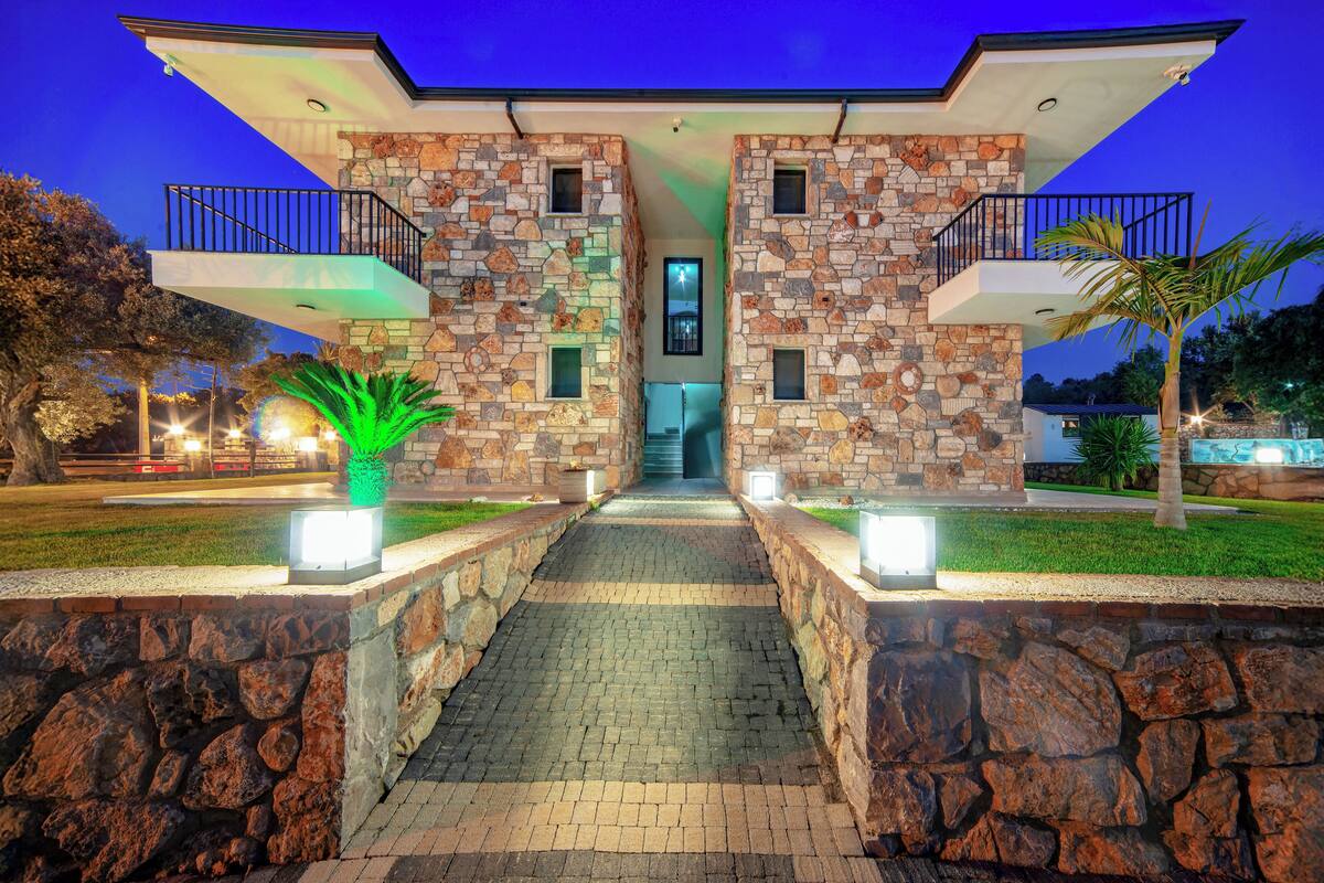 A modern house with a stone facade, a central entrance, and a pathway leading to the front door.
