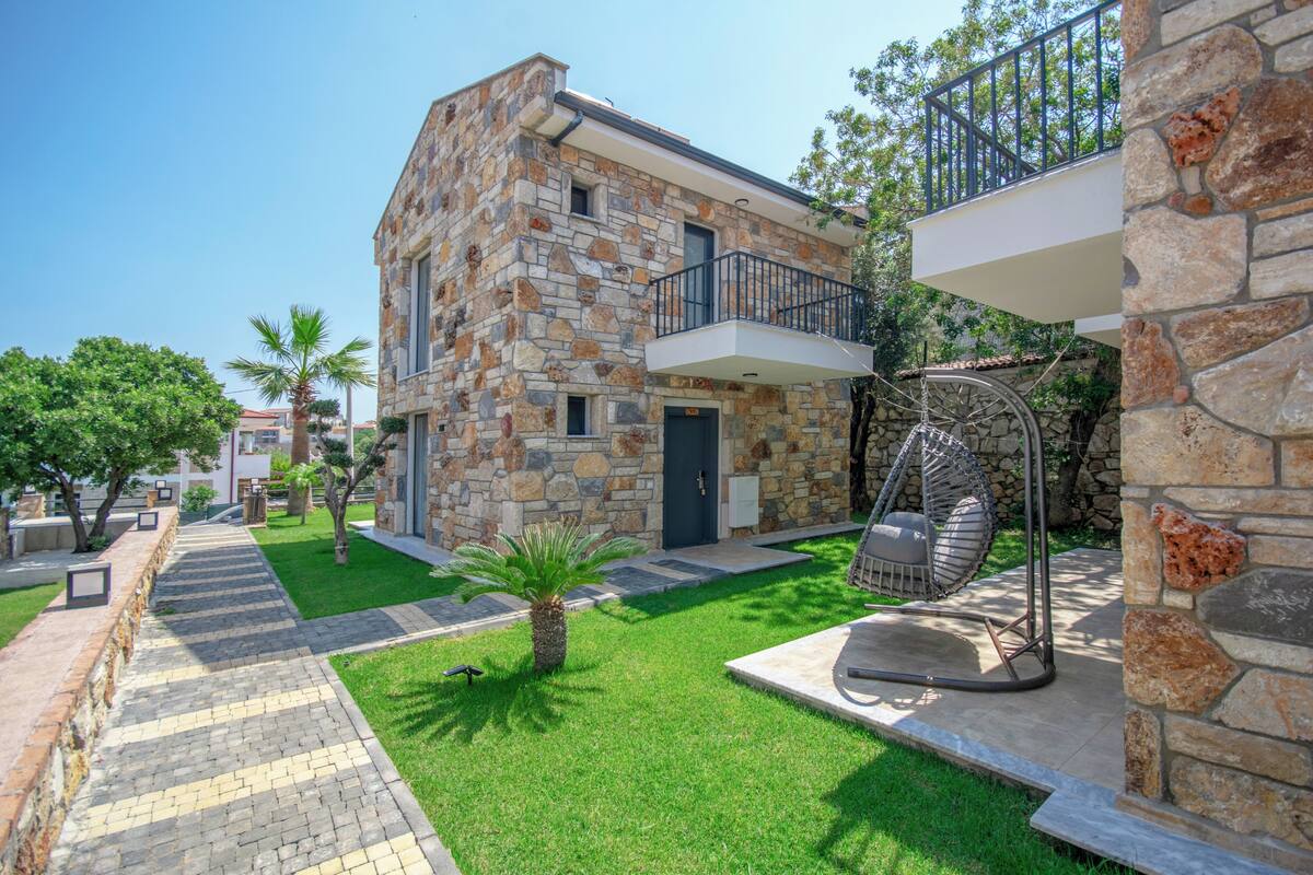 A stone building with a balcony, a swing chair, and a well-maintained lawn.