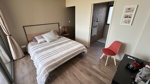 A hotel room with a bed, a red chair, a desk with a model car, and a door leading to a bathroom. - Maison vue de mer Pléneuf Val André near coastal paths and beaches (Pléneuf-Val-André)