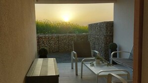 A patio with a table and chairs, a stone wall, and a view of a field with the sun setting in the background. - Maison vue de mer Pléneuf Val André near coastal paths and beaches (Pléneuf-Val-André)