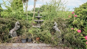 A garden with a stone fountain, potted plants, and statues. - Lilly's Bungalow (Clonakilty)
