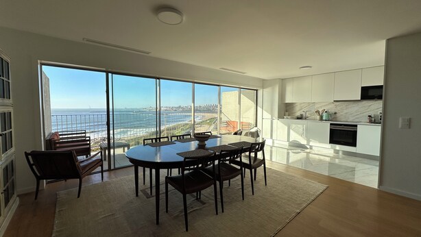 A modern kitchen with white cabinets and a marble backsplash, a dining area with a large table and chairs, and a view of the ocean through floor-to-ceiling windows. - Atlantis Ocean front (Vila Nova de Gaia)