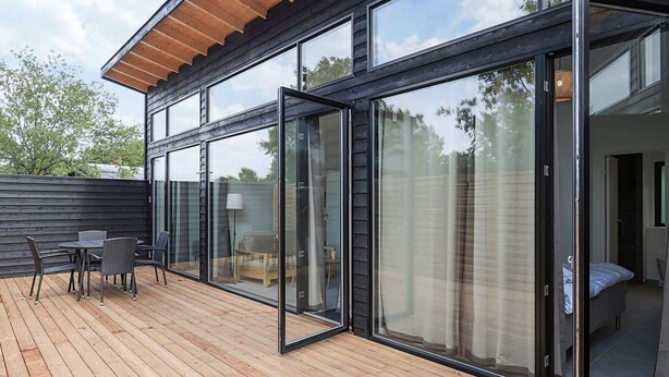 Uma casa moderna com grandes portas de vidro deslizantes que dão para um deck com móveis de exterior.