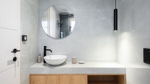Une salle de bain moderne avec un lavabo blanc, un miroir rond et un luminaire suspendu noir.