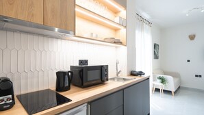 Une cuisine moderne équipée d’un four à micro-ondes, d’une machine à café et d’un four encastré. Elle est dotée d’un plan de travail en bois et d’un crédence carrelée blanche.