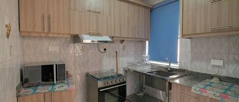 A compact kitchen with wooden cabinets, a microwave, a stove, and a sink.
