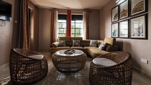 A living room with a sofa set, two wicker chairs, a round coffee table, and a TV mounted on the wall. - Aqueduct 1359 Hotel Apartments (Kampala)