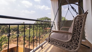 A wicker swing chair on a balcony with a view of greenery and hills. - Aqueduct 1359 Hotel Apartments (Kampala)
