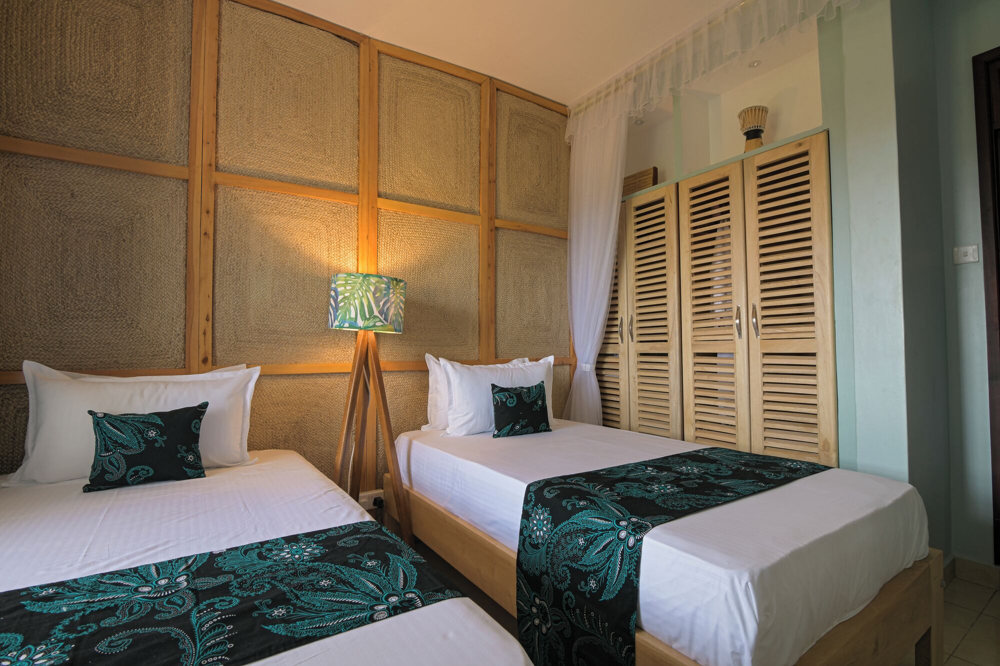 Habitación de hotel con dos camas, una lámpara de pie y armarios de madera.