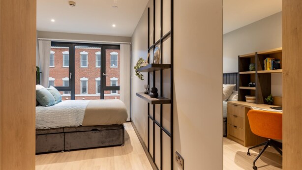 A modern bedroom with a large window, a bed, a desk, and a bookshelf. - Student Only Port on the Square (Bristol)