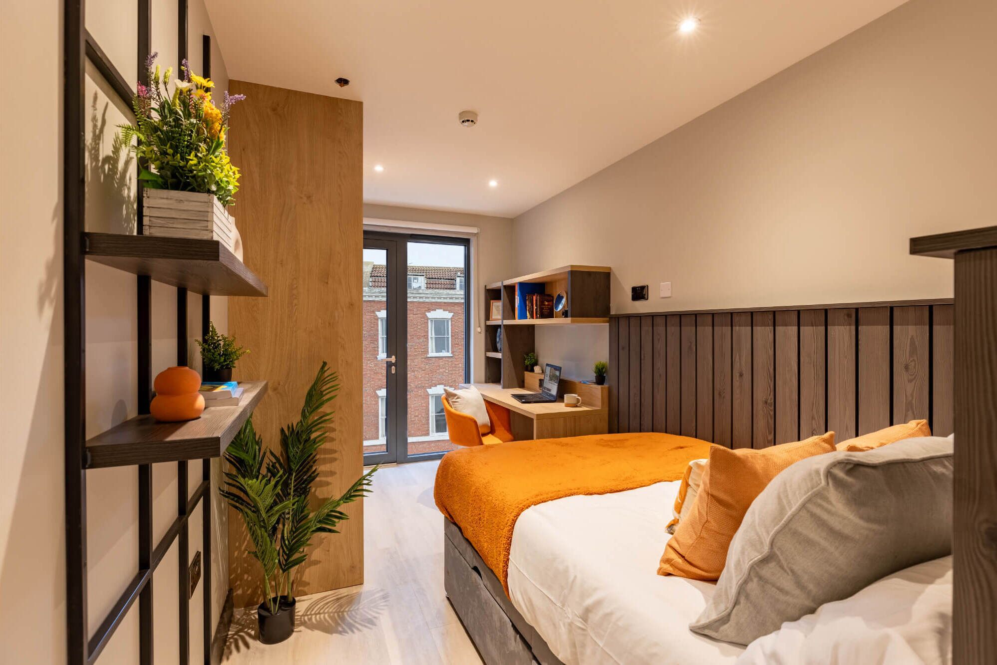 A modern bedroom with a bed, a desk, and a bookshelf.