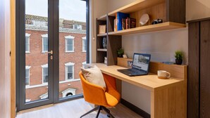 A modern office space with a desk, laptop, and shelves with books and decorative items. - Student Only Port on the Square (Bristol)
