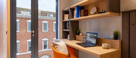 Un espace de bureau moderne comprenant un bureau, un ordinateur portable et des étagères remplies de livres et d’objets décoratifs.