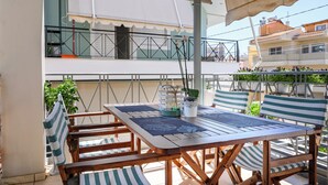 An outdoor patio with a wooden table and striped chairs, a potted plant, and a view of a building with balconies. - Lovehome-4BD Villa with views,dinners-close to airport, MEC ΑΕ,bus stop, Railway (Gerakas)