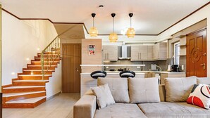 A modern living room with a wooden staircase, a sofa with cushions, and pendant lighting. - Lovehome-4BD Villa with views,dinners-close to airport, MEC ΑΕ,bus stop, Railway (Gerakas)