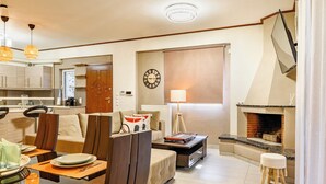 A modern living room with a sofa, coffee table, and dining area. There is a fireplace and a clock on the wall. - Lovehome-4BD Villa with views,dinners-close to airport, MEC ΑΕ,bus stop, Railway (Gerakas)