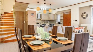 A modern kitchen with wooden cabinets, a dining area with a glass-top table, and a staircase with a metal railing. - Lovehome-4BD Villa with views,dinners-close to airport, MEC ΑΕ,bus stop, Railway (Gerakas)