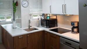 Una cocina moderna con armarios blancos, un refrigerador de acero inoxidable, un horno empotrado y una cafetera.