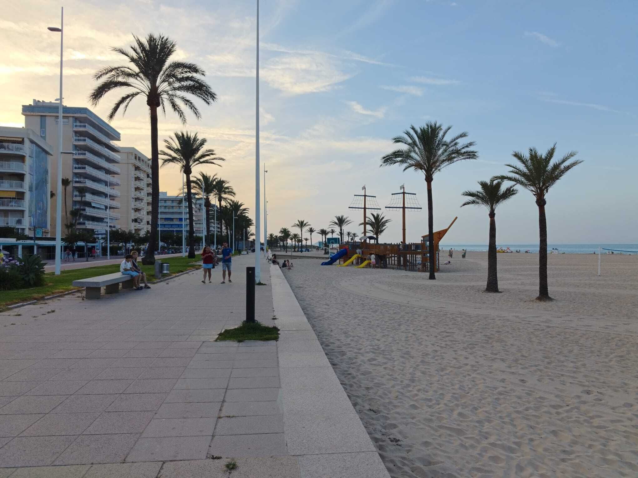 A beach promenade with palm trees, a playground, and a building with balconies.