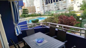 Un balcón con mesa y sillas, con vista a una piscina y edificios residenciales.