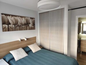 A bedroom with a bed, a headboard, a wall-mounted light fixture, a painting, and a sliding door.