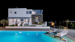 A modern two-story house with a swimming pool, outdoor seating, and a well-lit patio area. - Golden Sunrise Suites - Santorini Lux Family Suite (Santorini)
