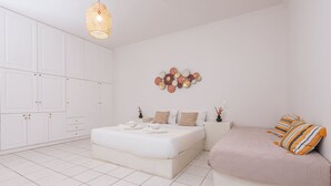 A bedroom with a large bed, a sofa, a wardrobe, and a wall art piece. - Golden Sunrise Suites - Santorini Family Suite (Santorini)