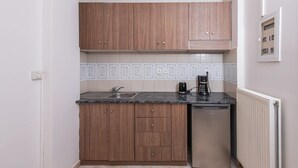 A compact kitchen with wooden cabinets, a sink, a coffee maker, and a dishwasher. - Golden Sunrise Suites - Santorini Family Suite (Santorini)