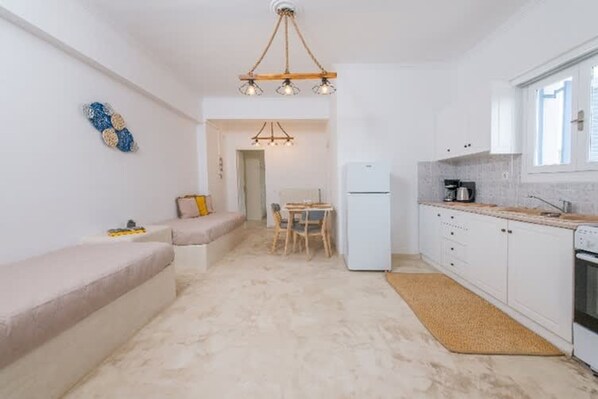 Una cocina compacta con armarios blancos, horno integrado, cafetera y comedor con mesa y sillas.