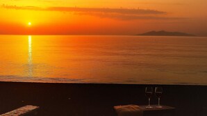 Vista del atardecer desde un balcón con dos copas de vino tinto sobre una mesita.