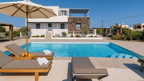 Un área de piscina moderna con sillones de descanso, una sombrilla y un edificio de fachada de piedra al fondo.
