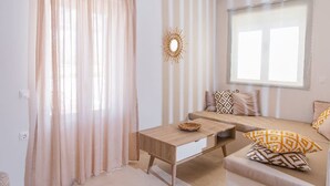 A room with a sofa, a coffee table, and a window with curtains. - Golden Sunrise Suites - Santorini Superior Suite (Santorini)