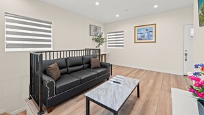 A modern living room with a black leather sofa, a marble coffee table, and wooden flooring. - Modern Getaway Near Pasadena Dtla (Rosemead)