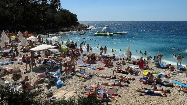 A crowded beach with people sunbathing and swimming, and a boat in the water.