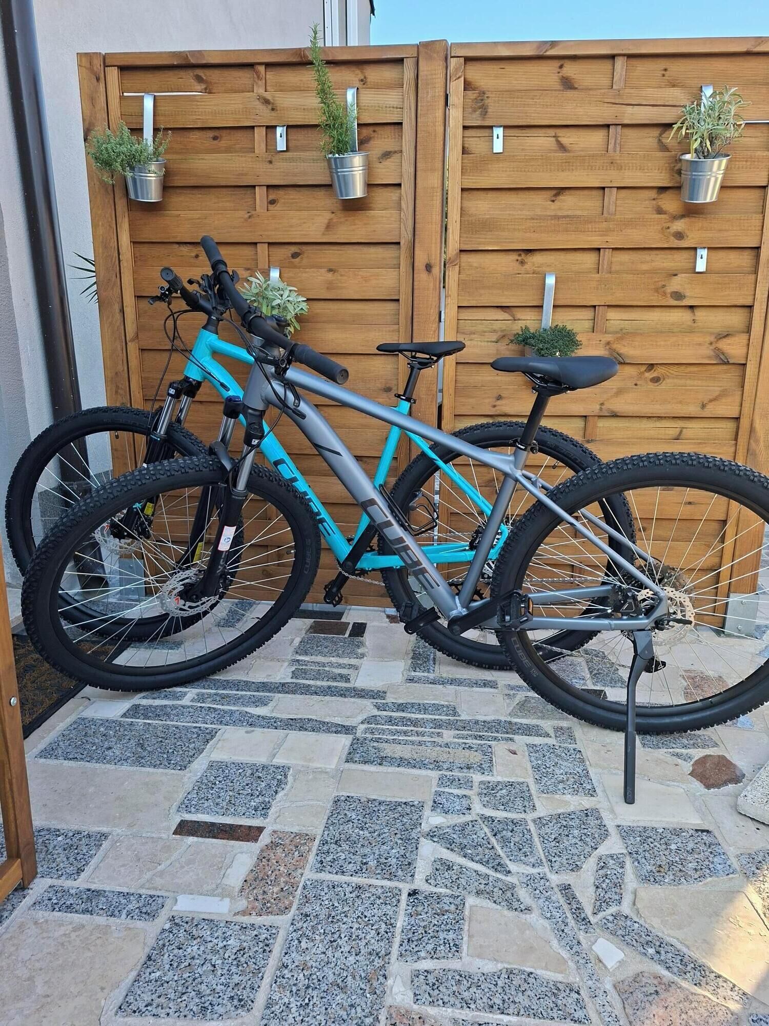 A turquoise mountain bike parked on a stone patio with a wooden fence and potted plants in the background.