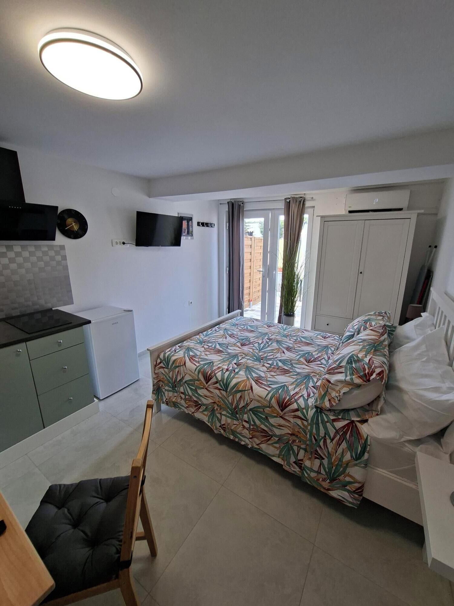 Un dormitorio moderno con cama, escritorio, silla, televisor y una kitchenette pequeña.
