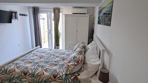 A bedroom with a bed, a bedside table with a lamp, a painting on the wall, and a door leading to a balcony.