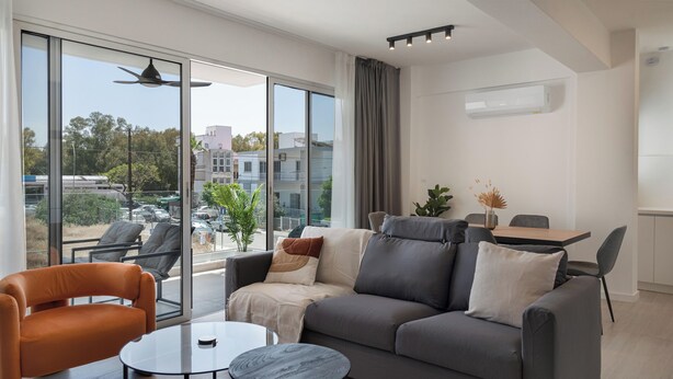 A modern living room with a grey sofa, orange armchair, and a glass coffee table. - Phaedrus Living: Travertine Residences 101 (Strovolos)