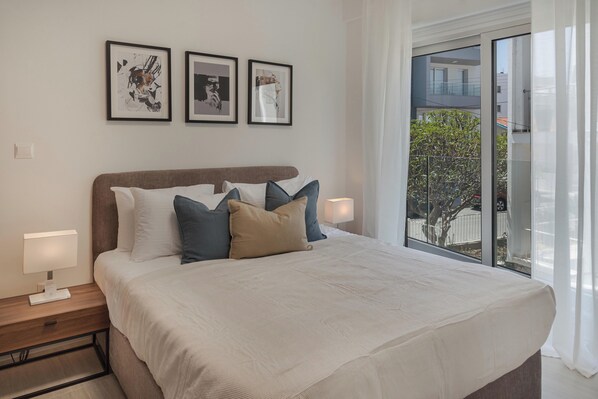 A neatly made bed with a white comforter and multiple pillows, a bedside table with a lamp, and three framed artworks on the wall. - Phaedrus Living: Travertine Residences 101 (Strovolos)