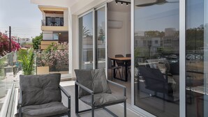 A balcony with two chairs and a table, a sliding glass door leading to an indoor area, and a view of the cityscape. - Phaedrus Living: Travertine Residences 101 (Strovolos)