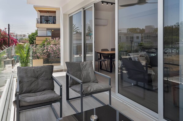 A balcony with two chairs and a table, a sliding glass door leading to an indoor area, and a view of the cityscape. - Phaedrus Living: Travertine Residences 101 (Strovolos)