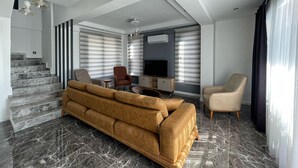 A modern living room with a sofa, chairs, a TV, and a staircase.