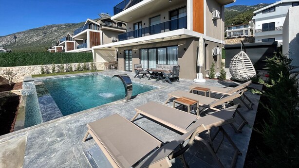A modern two-story house with a swimming pool, outdoor seating, and a view of the mountains.