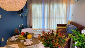 Un coin repas avec une table dressée pour deux personnes, un canapé et une grande fenêtre avec des rideaux.