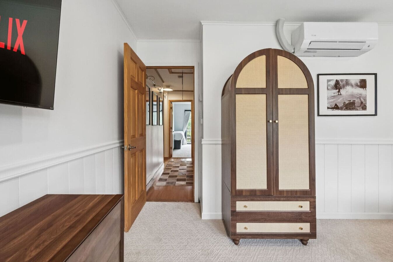 A hallway with a wooden cabinet, a television, and a framed picture on the wall.