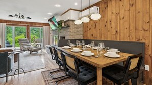 A dining area with a long wooden table set for six, surrounded by black upholstered chairs.