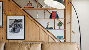 A cozy living room with a wooden staircase, a black floor lamp, and a framed photograph on the wall.