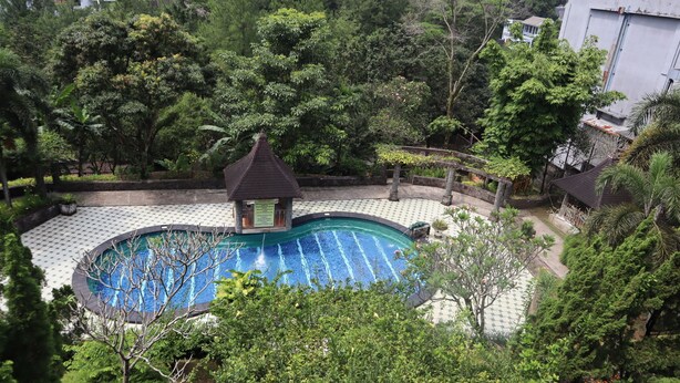 A swimming pool surrounded by lush greenery and a small pavilion. - Hotel Green Wattana Sentul (Citaringgul)