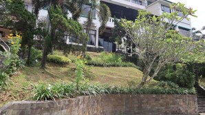 A landscaped garden with various plants and trees, a stone retaining wall, and a modern building with balconies in the background. - Hotel Green Wattana Sentul (Citaringgul)